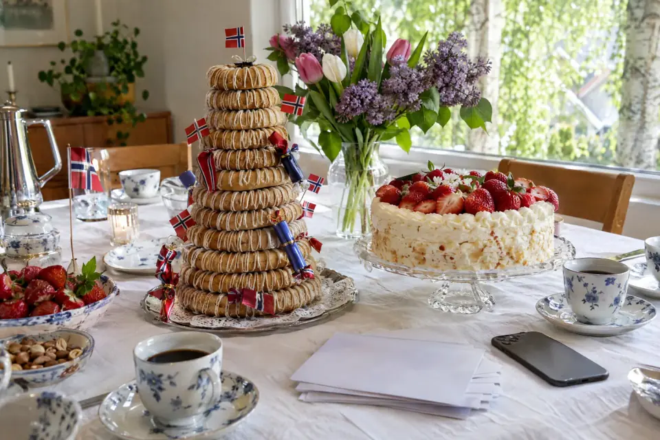Et konfirmasjonsbord: kransekake med små flagg, bløtkake, kaffekopper, tulipaner og en mobil på duken